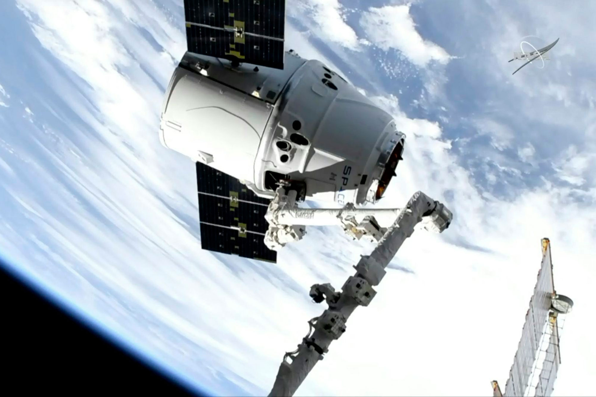 A conical white spacecraft with two rectangular solar panels in space, with the Earth in the background