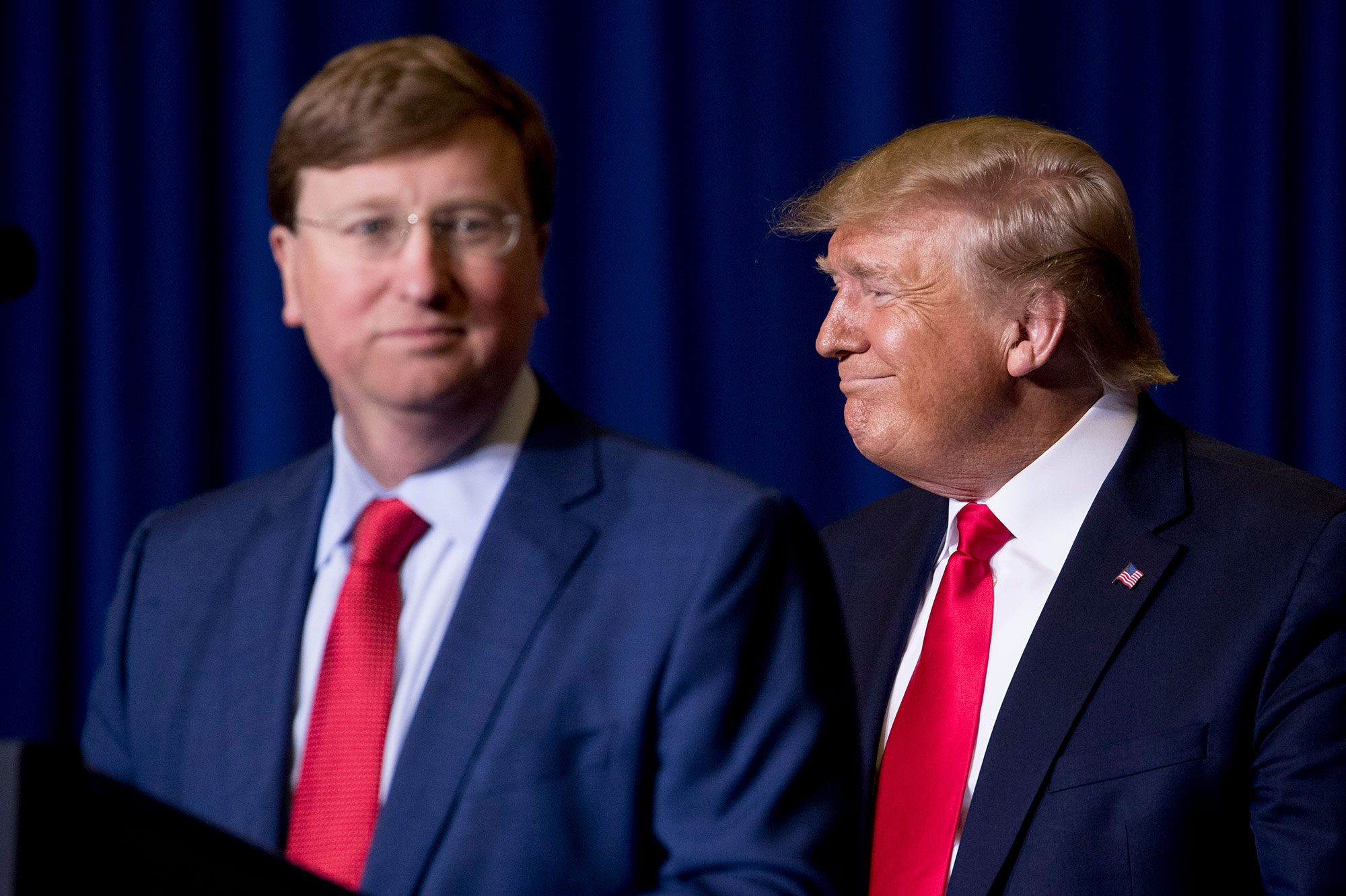 Tate Reeves and Donald Trump stand on stage in nearly matching navy suits with red ties