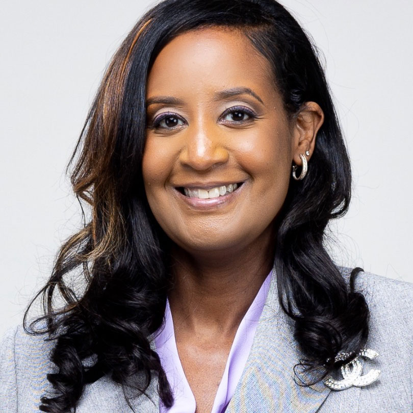 Headshot of a woman with long black curled hair wearing a grey jacket and