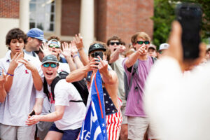 a white male ole miss students pointing, flipping the bird, laughing and holding a trump flag