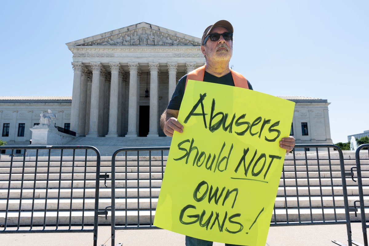 A man stands outside of the U.S. Supreme Court holding a bright yellow sign that says "Abusers should NOT own guns"