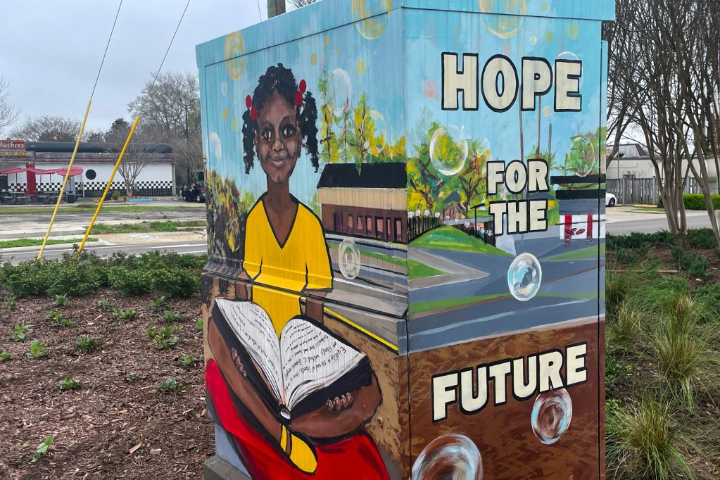 An outside utility box painted brightly with a student holding a book on one site and "Hope for the Future" on the other
