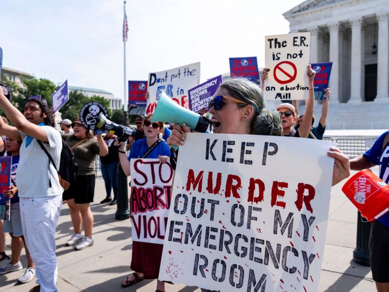Anti-abortion demonstrators protest outside the Supreme Court with signs that say things like "Keep murder out of my emergency room"