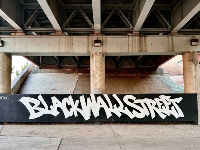 Graffiti under a bridge that reads "Black Wall Street" in white paint on a black background