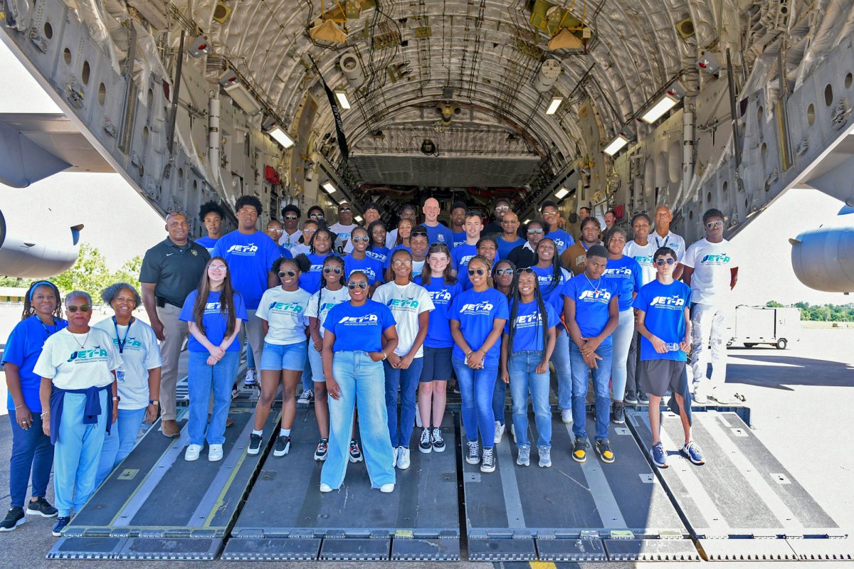 A large group of young adults in matching blue and white tshirts stand in the back of an open airplane