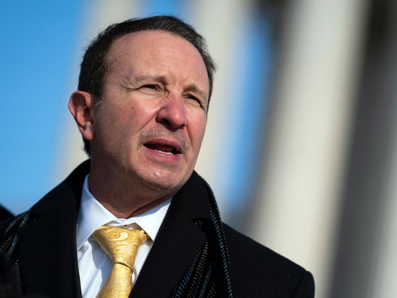 A man in a winter coat and tie stands outside