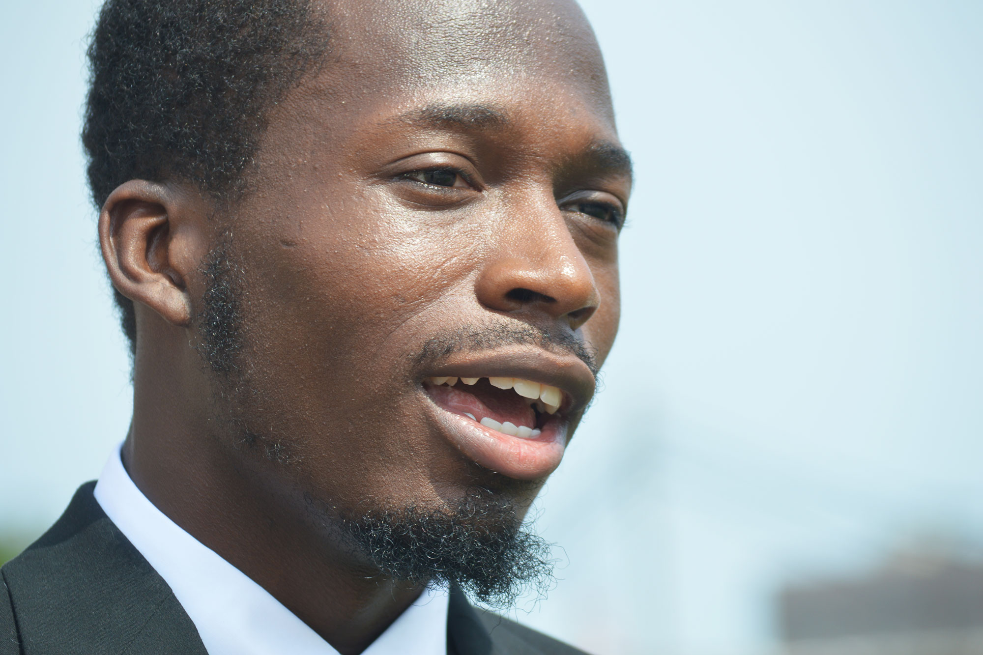 A younger man in a suit speaks outside