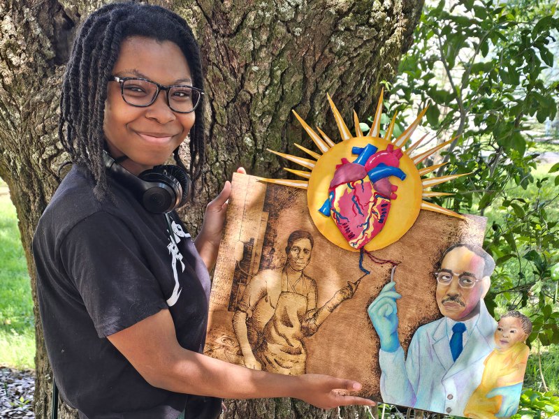 A student holds up a mixed media piece of art