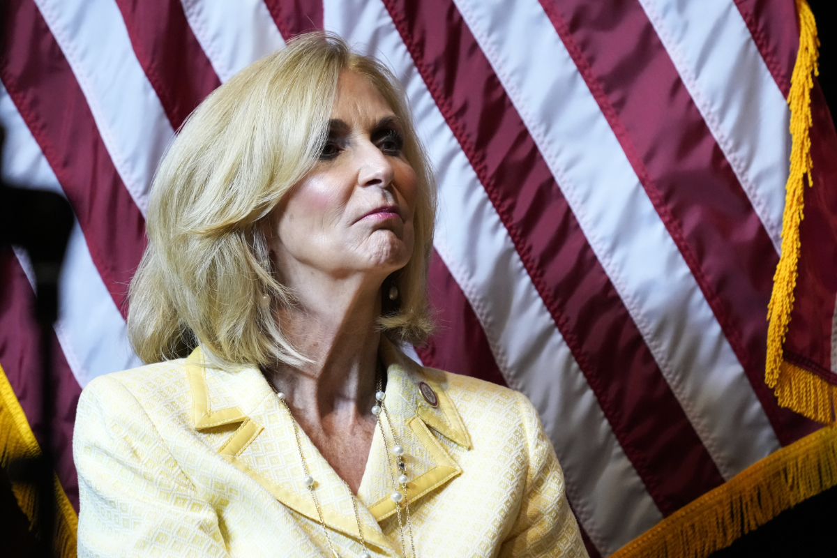 A woman in a yellow suit stands before the US Flag
