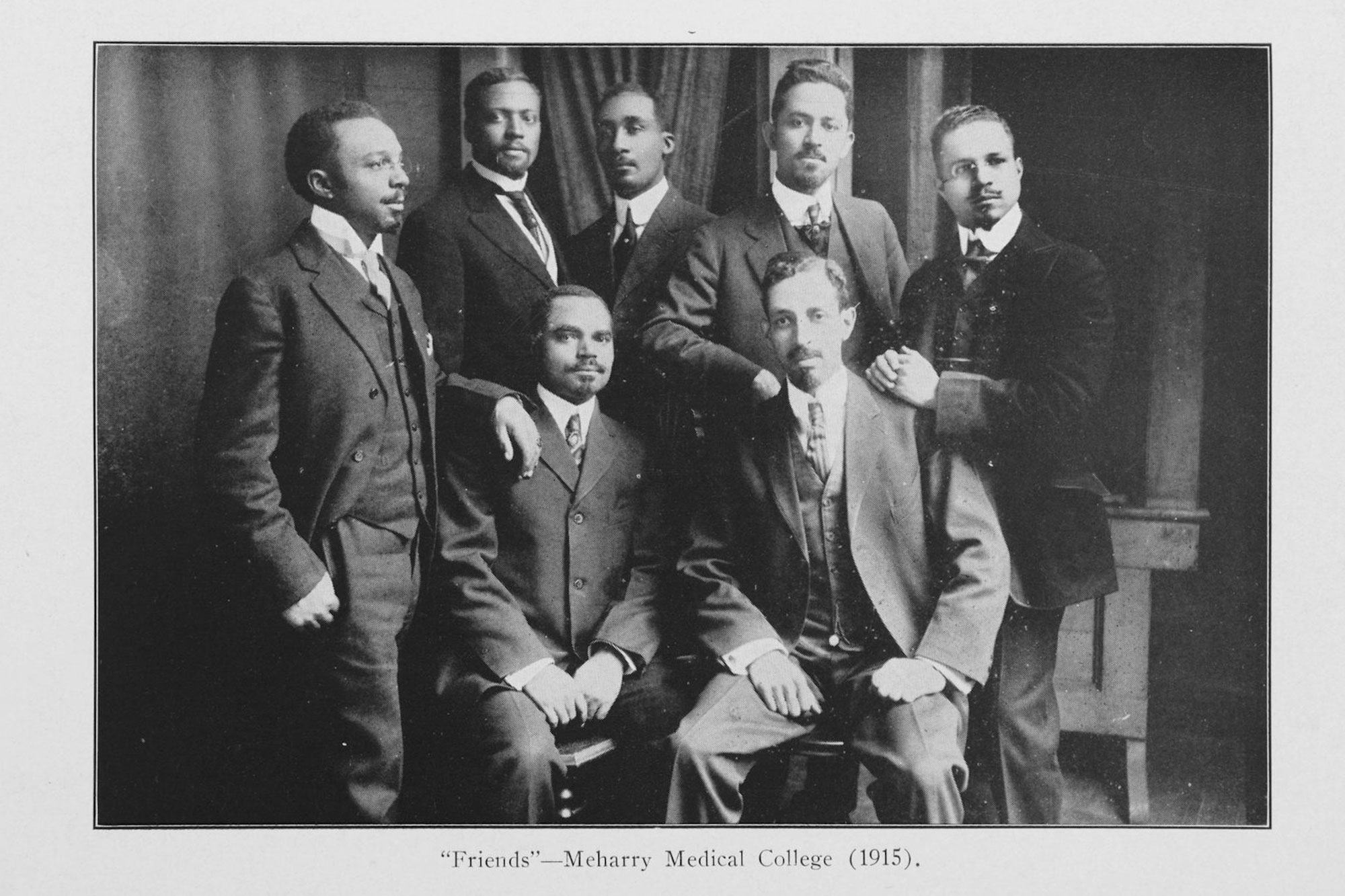 An old fashion black and white photo of 7 black men in suits posed together
