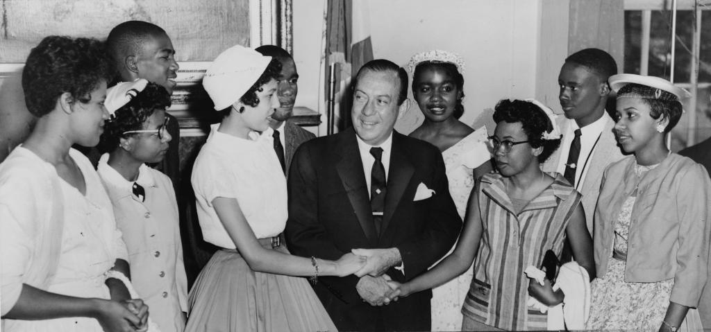 Nine young black people shake hands with a white man