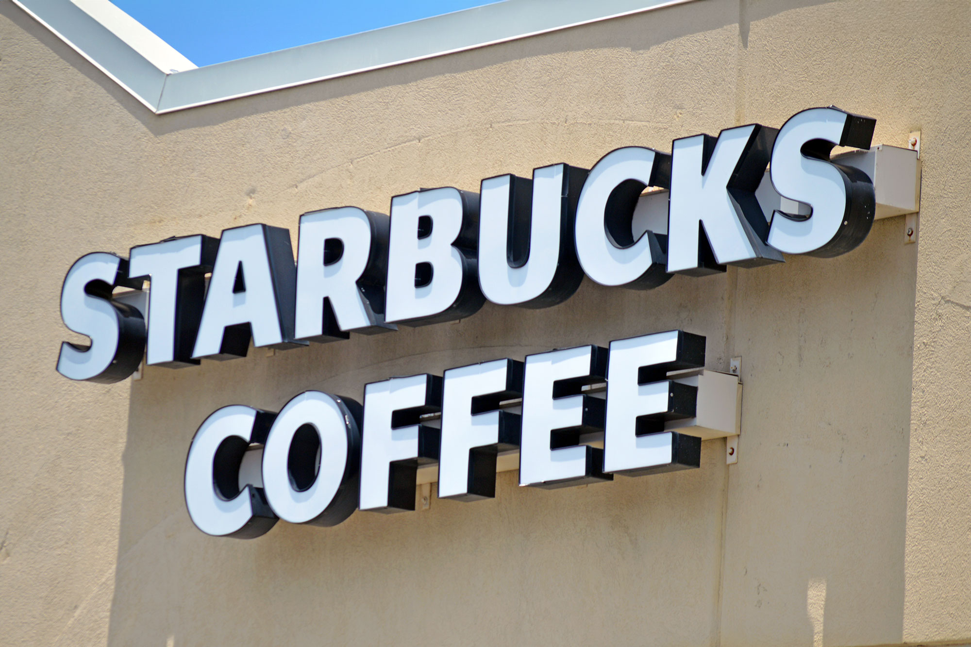A sign that reads Starbucks Coffee in white letters hung against a light brown store front wall