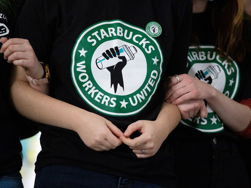 People in shirts that read "Starbucks Workers United" stand with arms linked