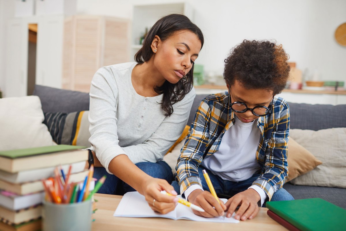 A woman tutors a child as they sit on a living room couch