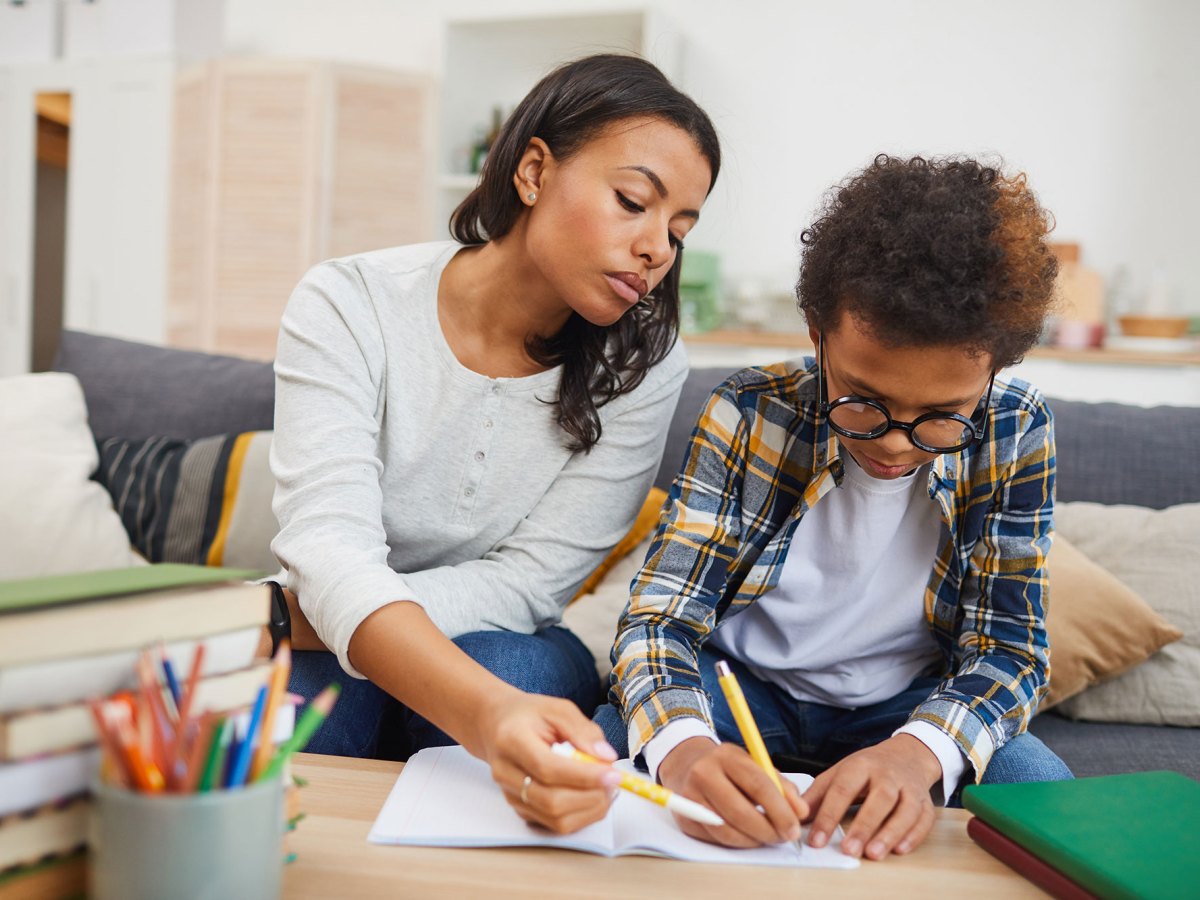 A woman tutors a child as they sit on a living room couch