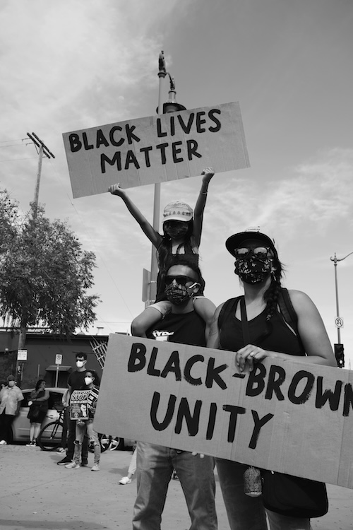 Three people holding up two different signs. One reads "Black Lives Matter" and the other says "Black-Brown Unity"