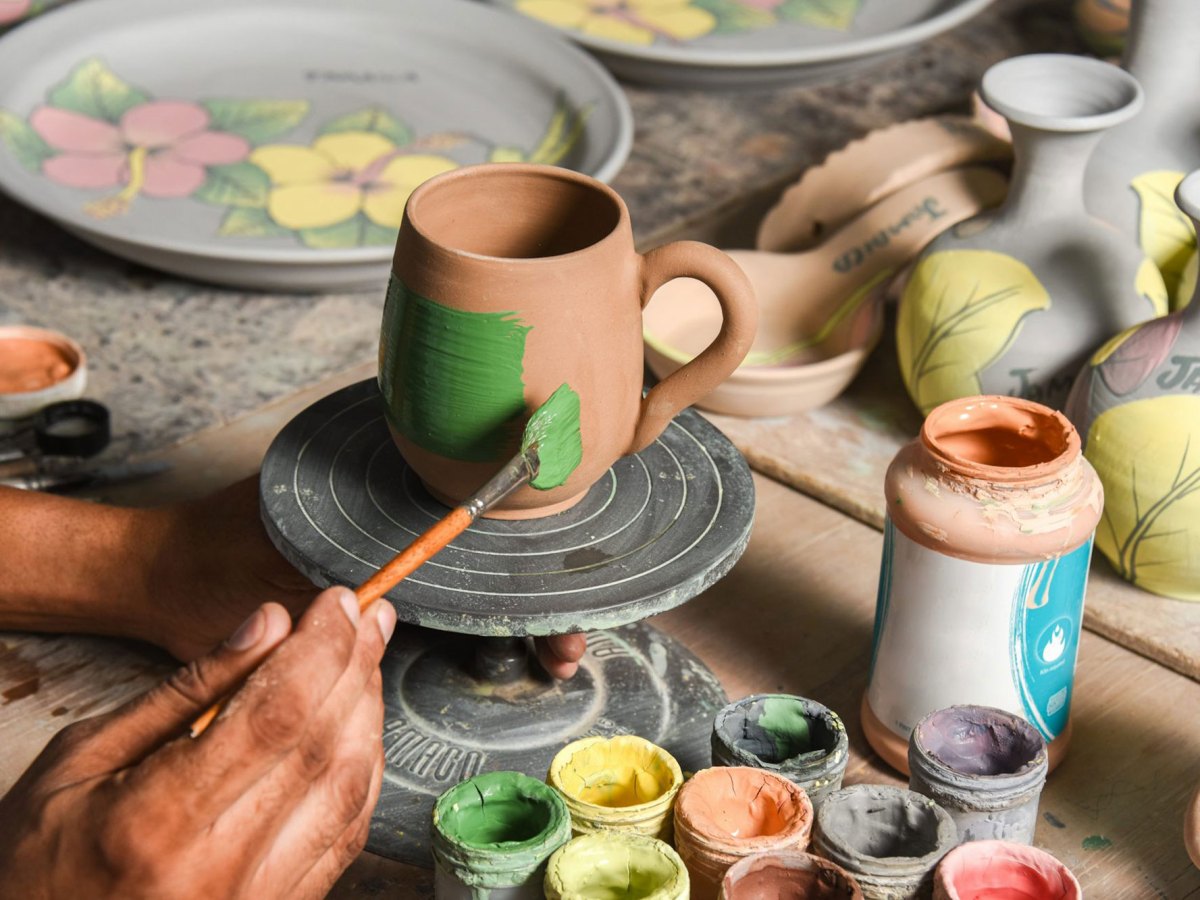 A hand is painting a pottery made cup green