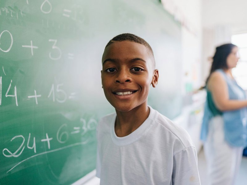 A student stands in front of a chalk board with math written on it