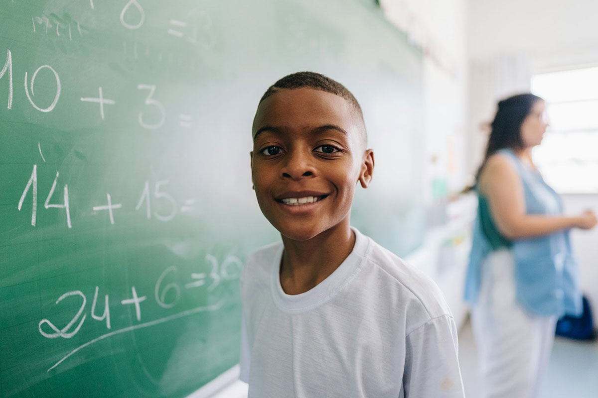 A student stands in front of a chalk board with math written on it