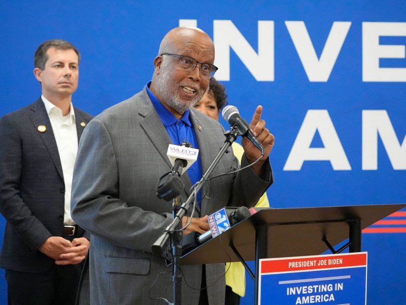 A man speaks at a podium labeled "President Joe Biden Investing in America"