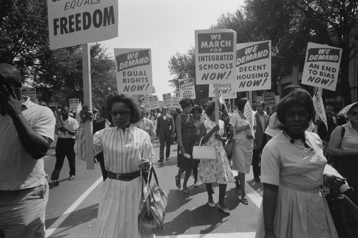 A group of black people march down the road with signs that ready We Demand Equal Rights Now!