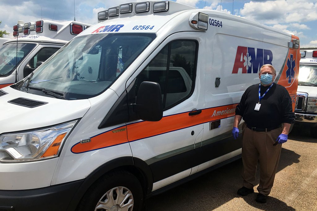 A man stands in front of a white and orange ambulance