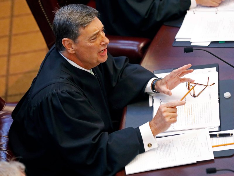 An above view of a judge seated at a table with papers before him, talking