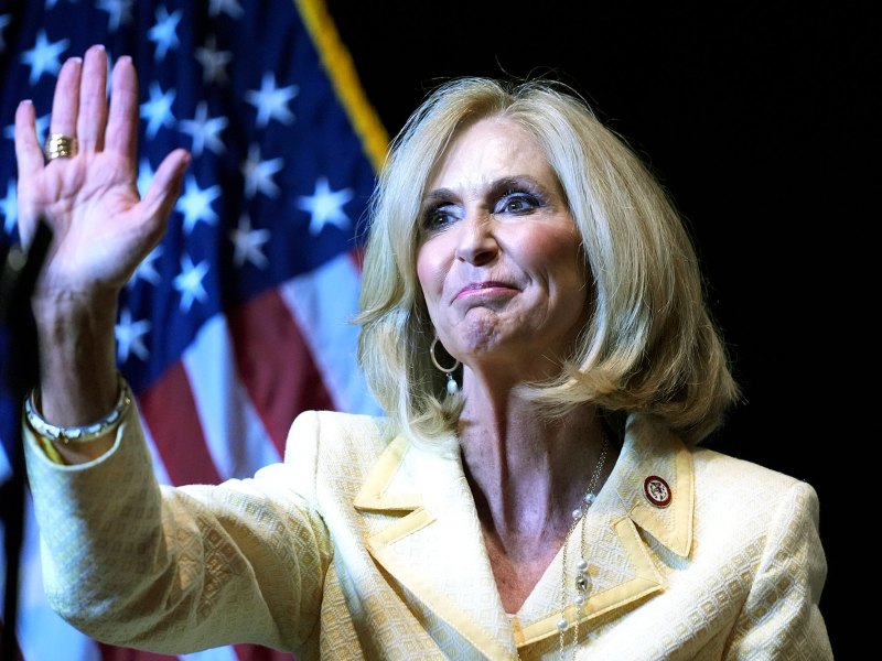 A woman in yellow waves on stage before a US Flag