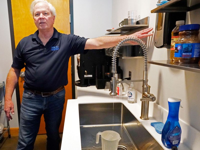 A man points at the wall over a dripping kitchen sink