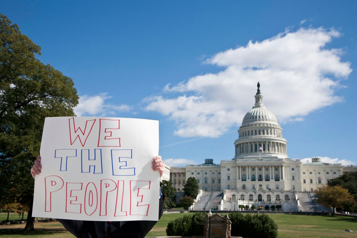 A person holds a handwritten sign that says "We the People" while they stand in front a capitol building