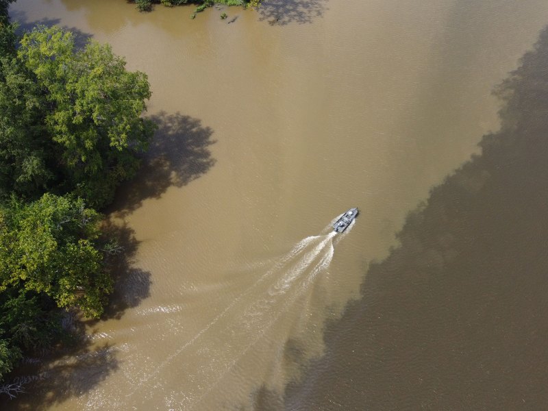 An overhead view of a speedboat driving through a muddy river