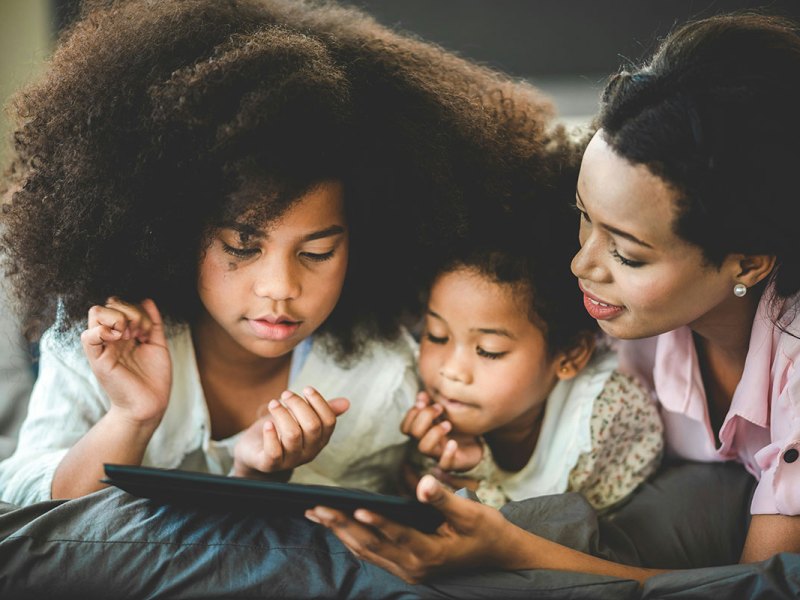 A mother looks at a tablet with her two children