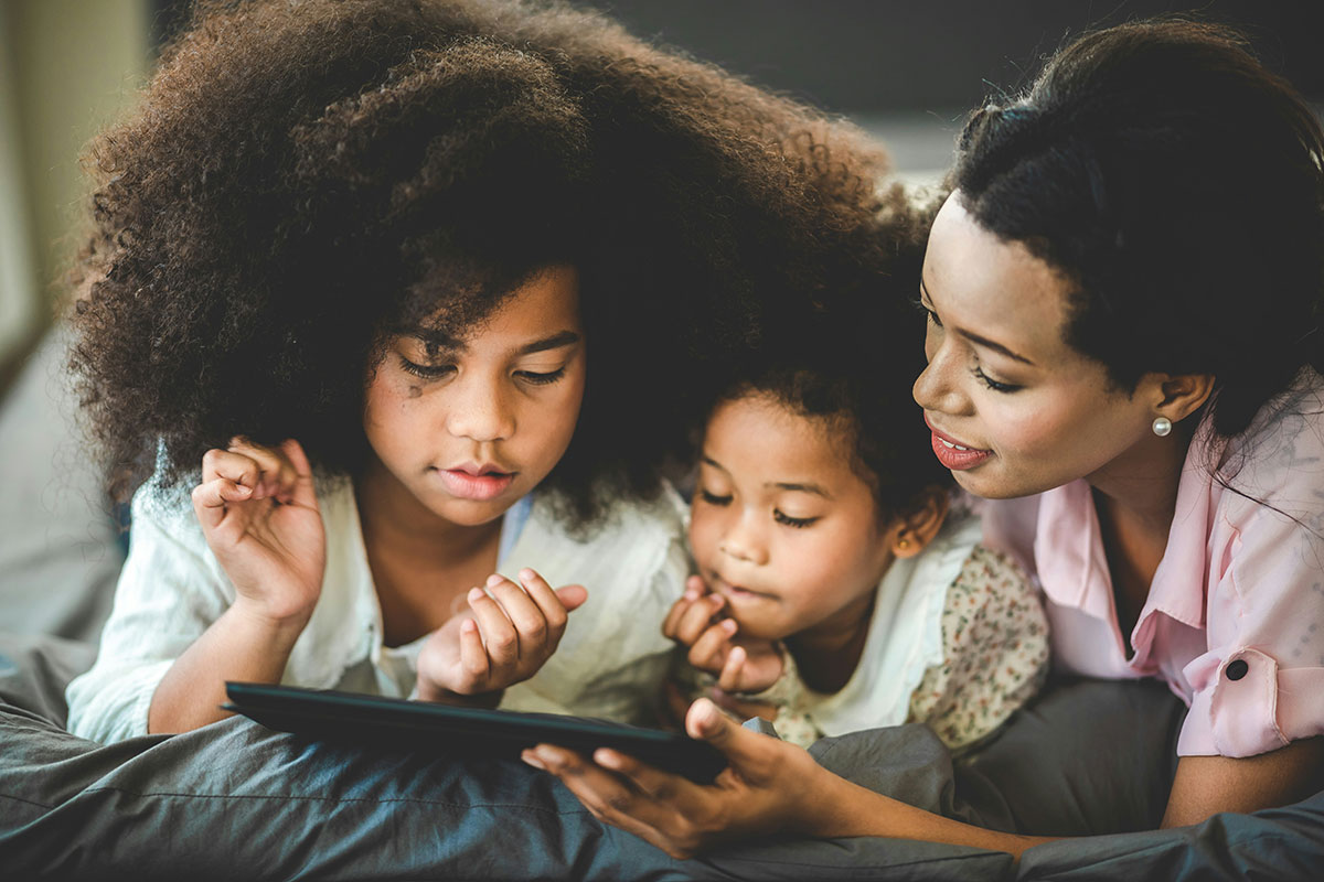 A mother looks at a tablet with her two children