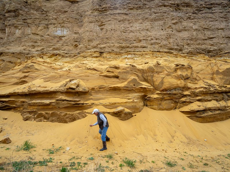 a photo shows a man picking up sand from a rockface
