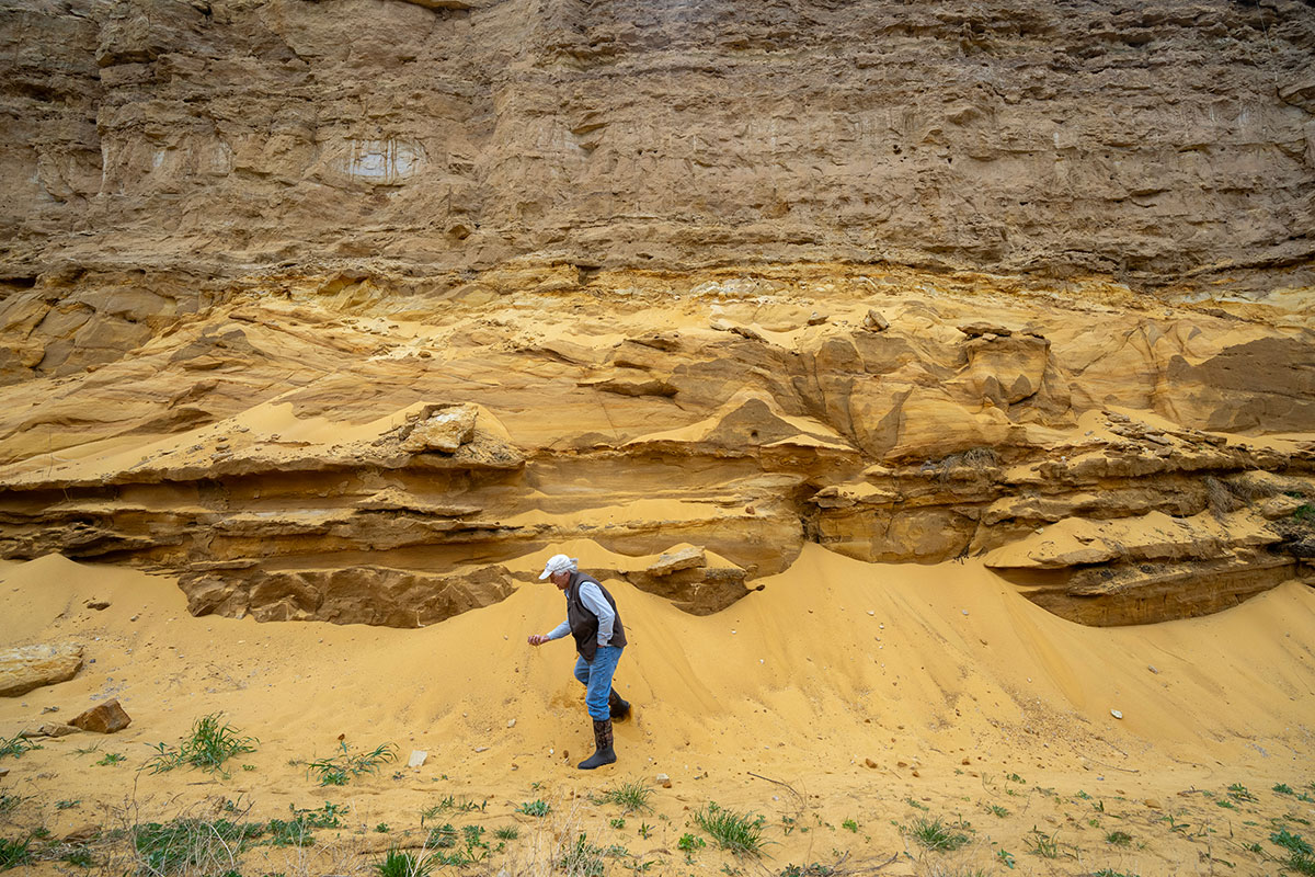 a photo shows a man picking up sand from a rockface