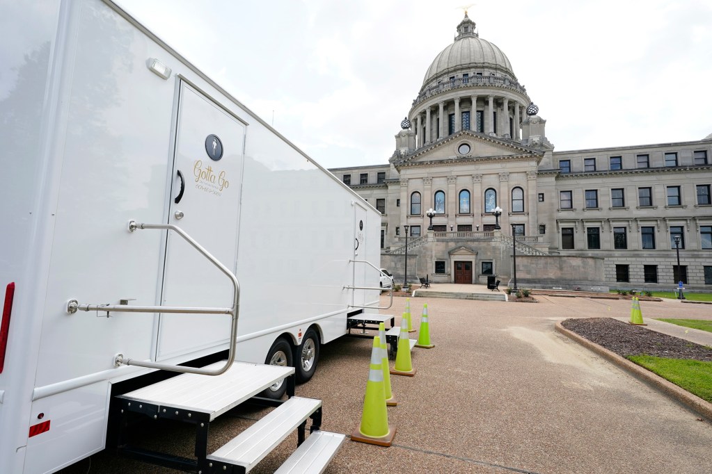 A view of a white truck with portable toilets parked in front of the state's Capitol building