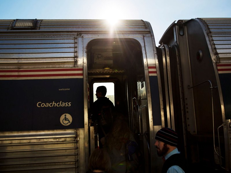 An exterior view of a silver Amtrak Train being boarded by two people