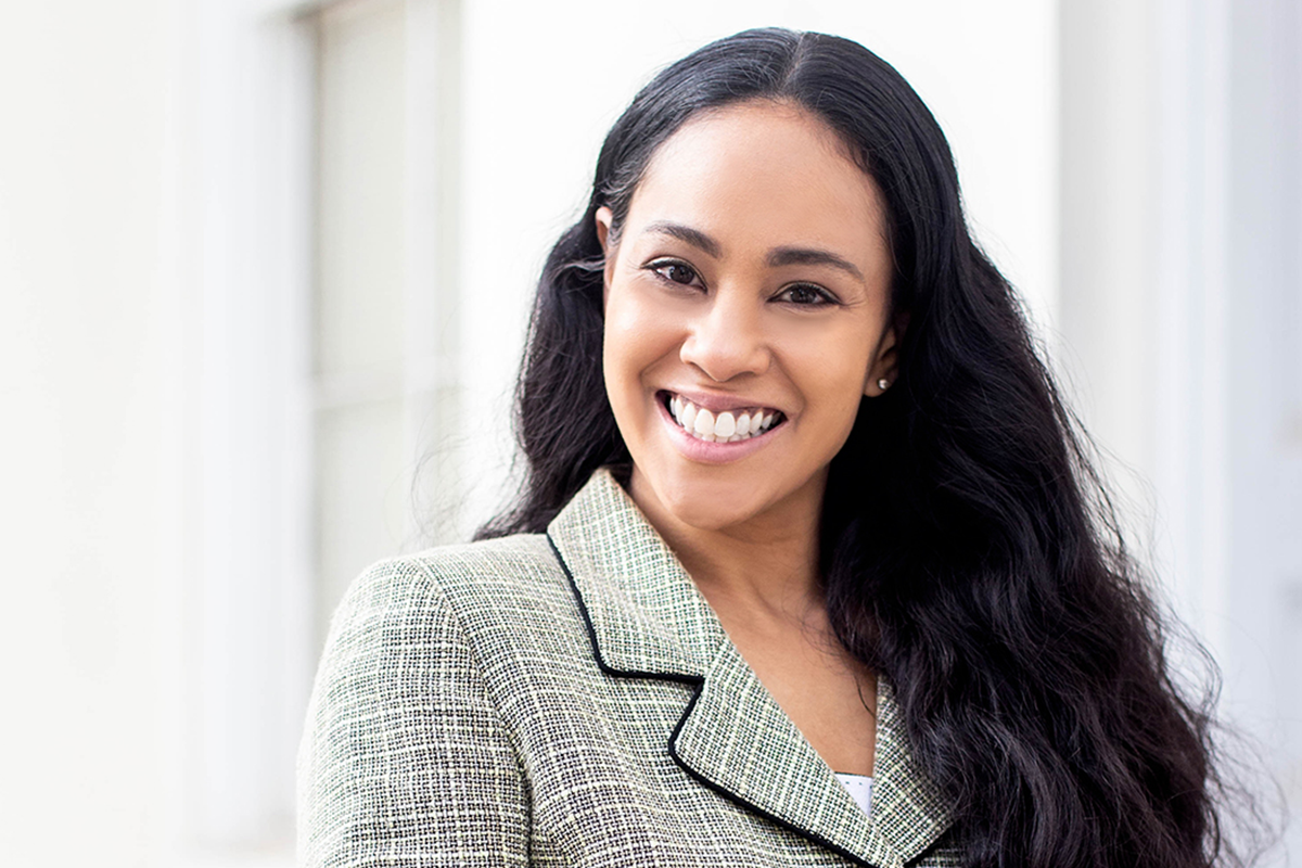 A photo of a smiling woman with long black hair and grey suit top standing outside