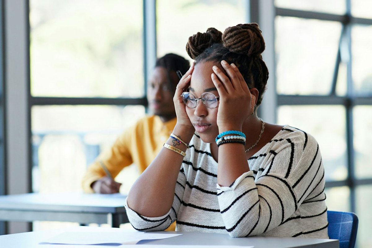 A student puts her hands on her head while sitting at a classroom desk