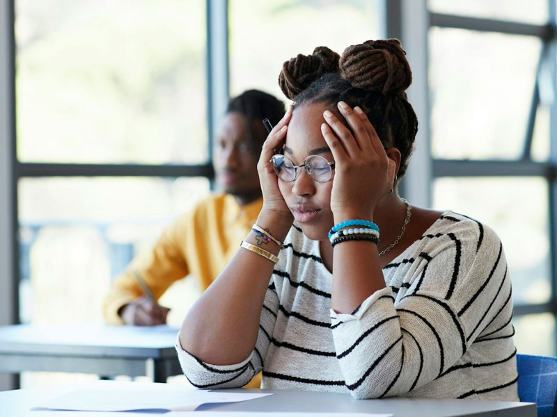 A student puts her hands on her head while sitting at a classroom desk