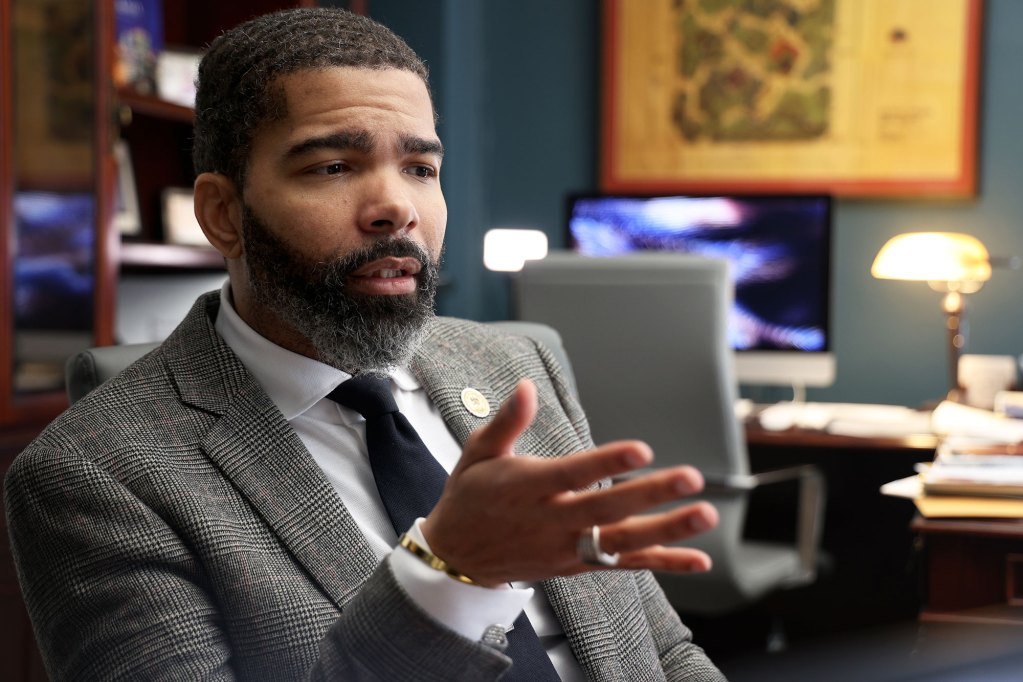 Mayor Lumumba sitting in his office, wearing a grey suit and speaking