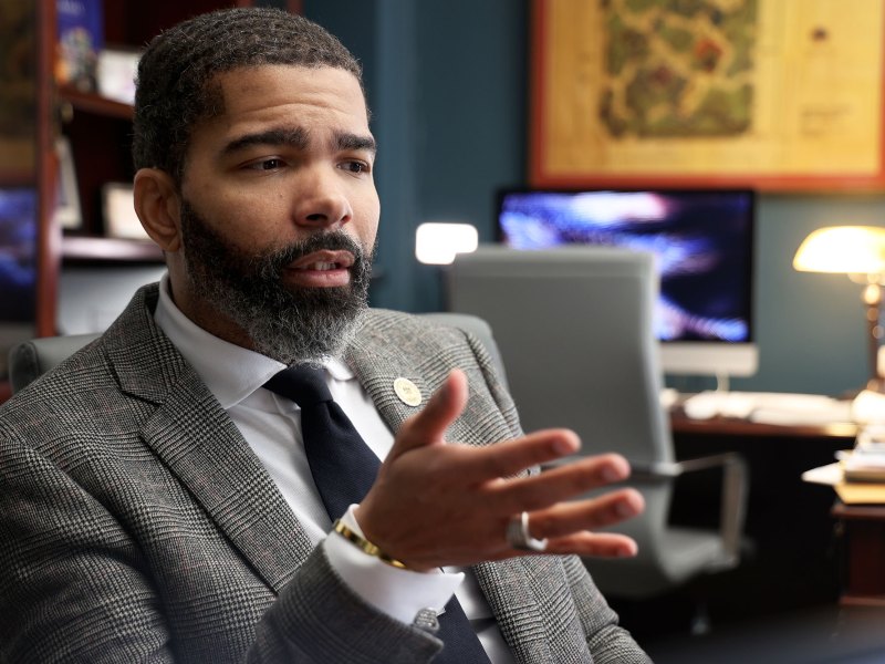 Mayor Lumumba sitting in his office, wearing a grey suit and speaking