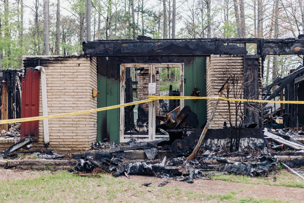 A light brick home destroyed by fire, the top half gone large sections of the walls, doors, and windows are missing