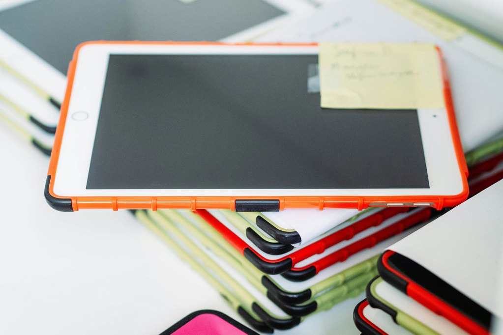 A stack of ipads sit on a table, each in primary colored cases