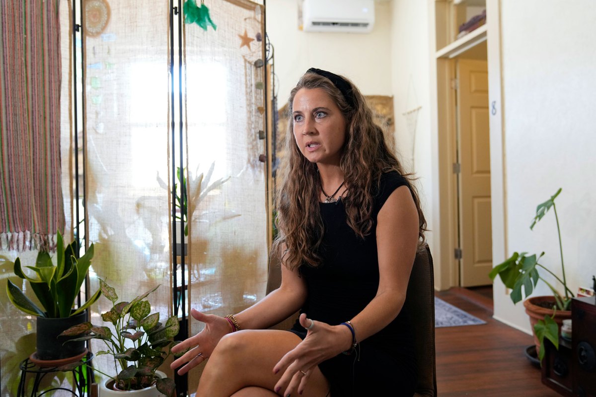 A woman in a black dress sits in a house filled with several potted plants