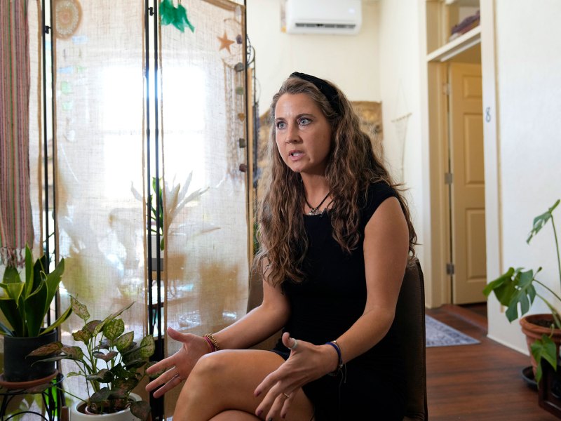 A woman in a black dress sits in a house filled with several potted plants