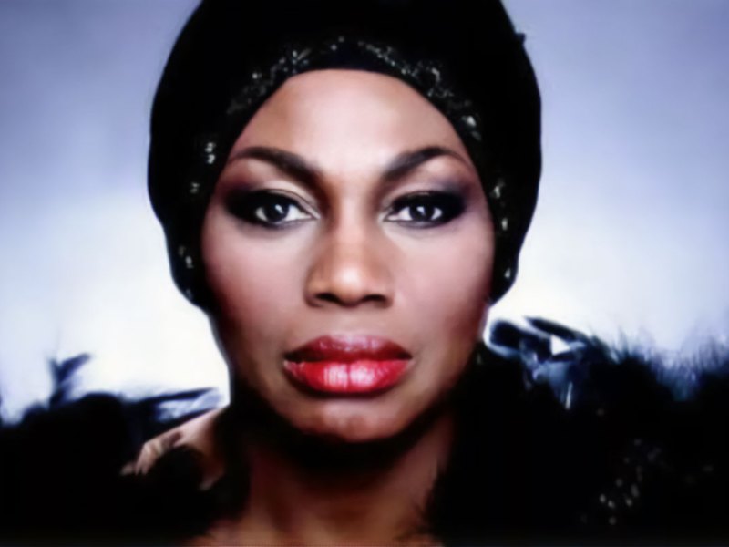 A glamor photo of a woman with a beaded black head wrap and black feathers on her shoulders