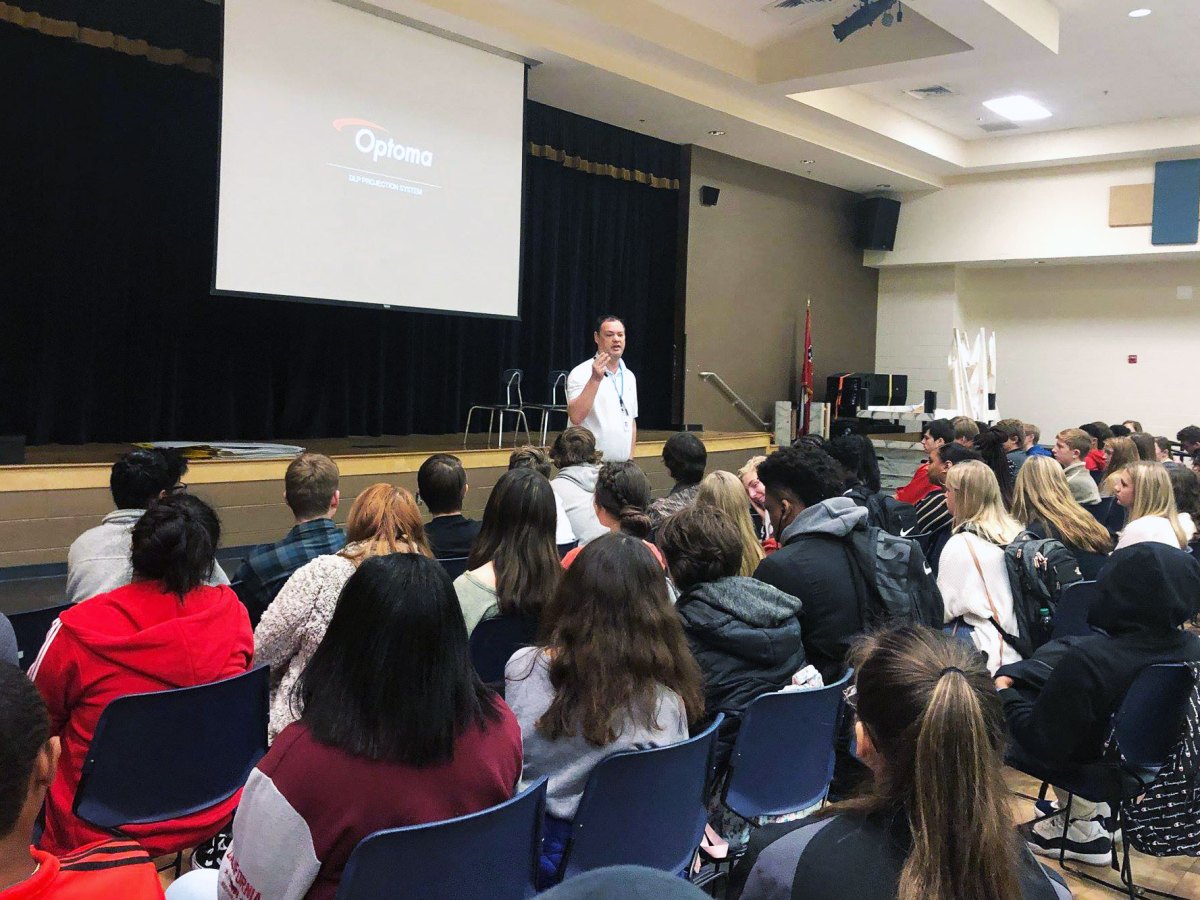 A man gives a presentation in front of rows of students in a school auditorium
