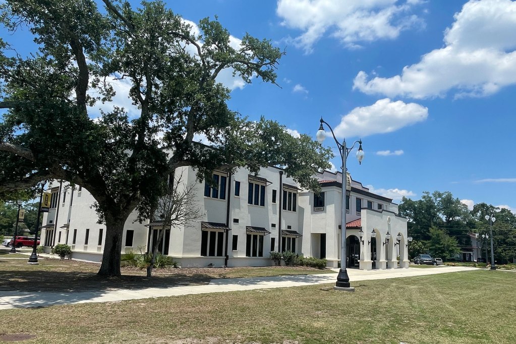 A white two story building is seen with a large tree to the left
