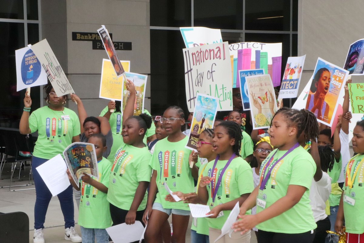 Students in bright green shirts hold signs outside of a building